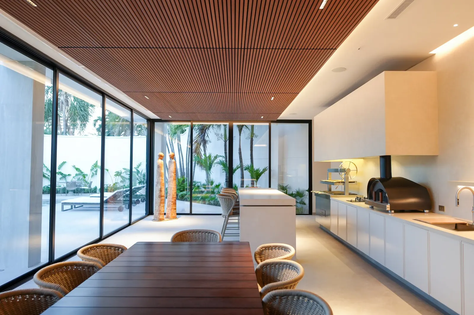 Vista del área social de la Casa AW: comedor de madera, isla, cocina con churrasquera y horno Averno, y ventanales que abren al jardín