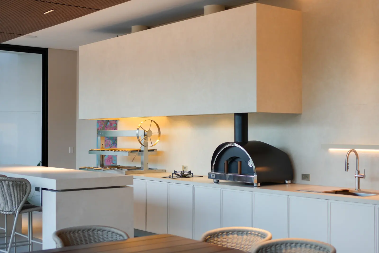 Churrasquera y horno Averno integrados a la cocina de la Casa AW, bajo una campana revestida en piedra clara