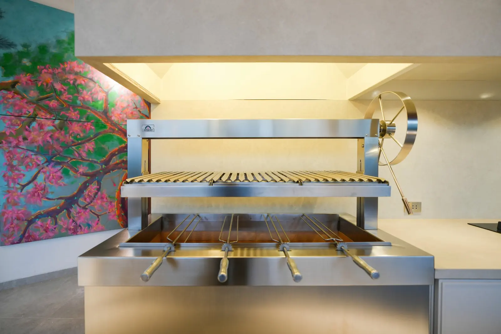 Detalle de la churrasquera Averno de la Casa AW, con parrilla elevada, volante de acero y brochetas