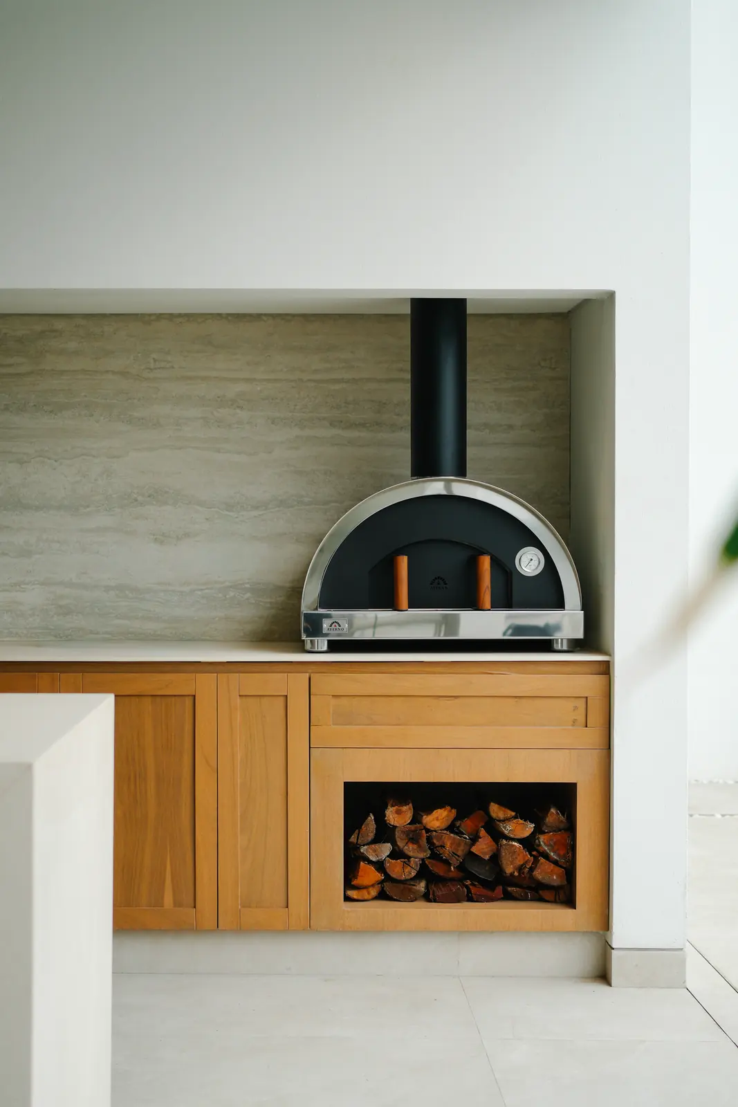 Horno Averno negro empotrado en un nicho de madera con leña guardada debajo