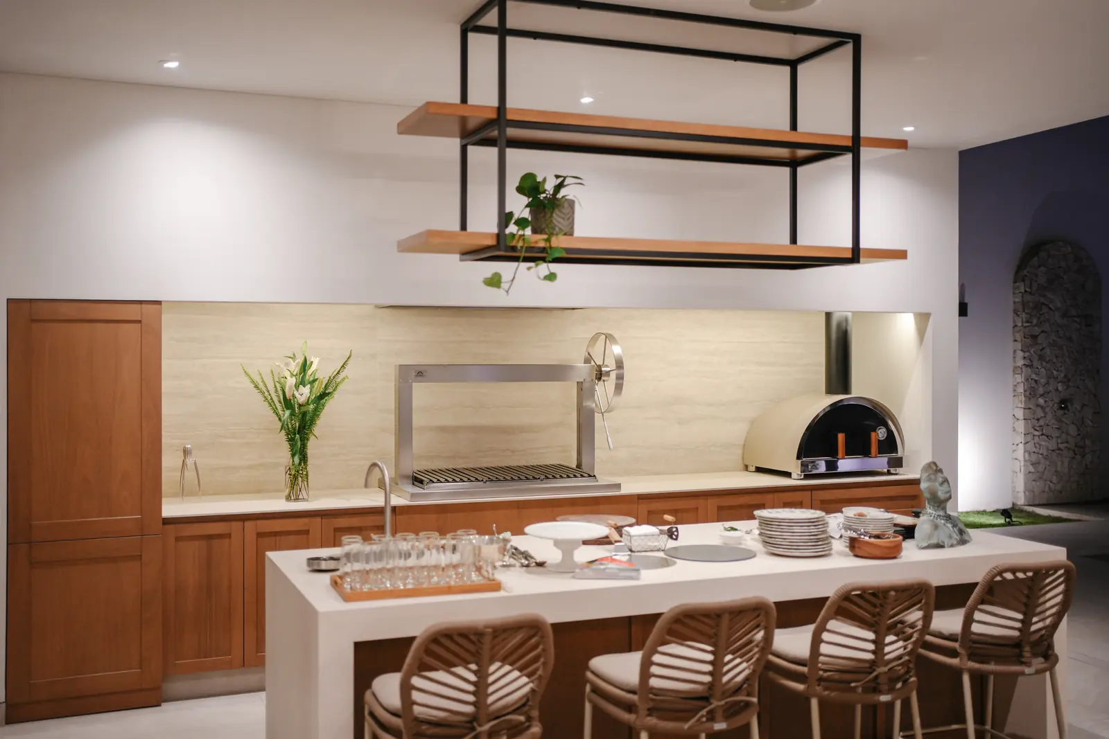 Cocina exterior de la Casa JG de noche, con churrasquera, horno y barra iluminados