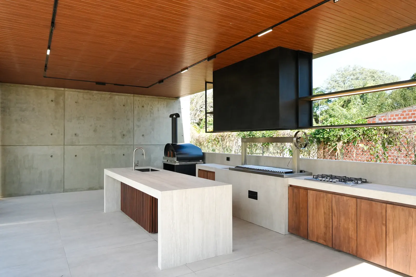 Interior del pabellón de la Quinta Porongo con isla de piedra clara, mesada de madera, churrasquera y campana negra suspendida