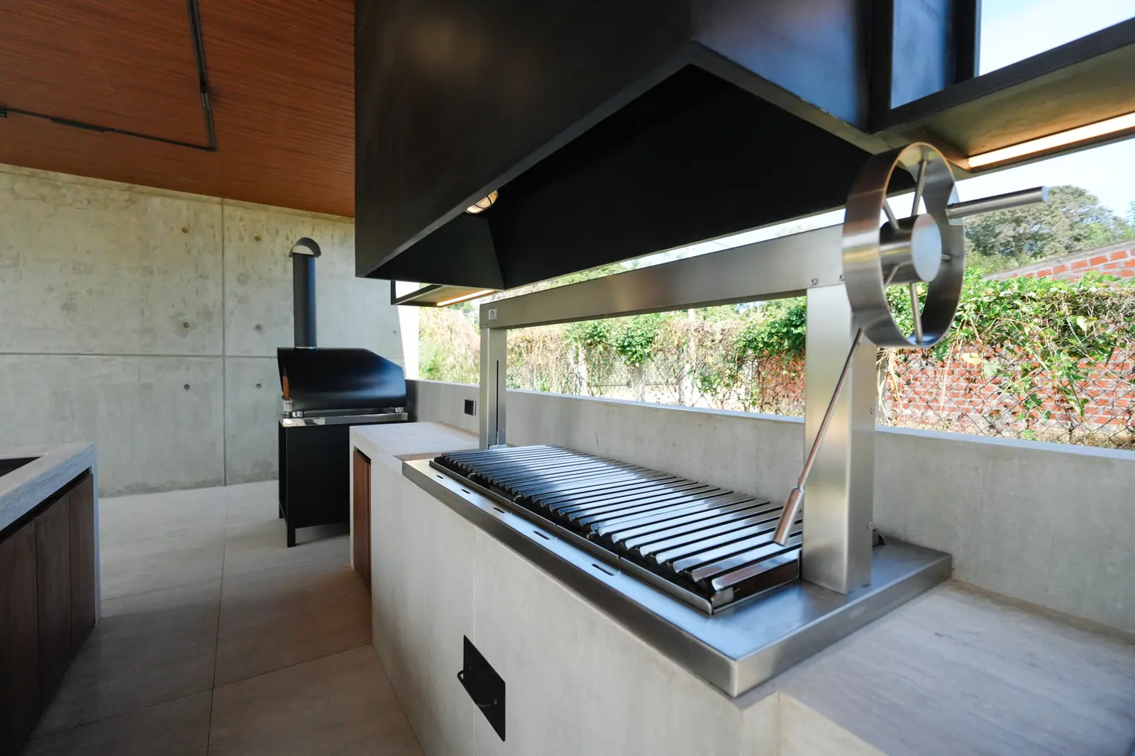 Churrasquera Averno con parrilla y volante de acero bajo la campana negra de la Quinta Porongo
