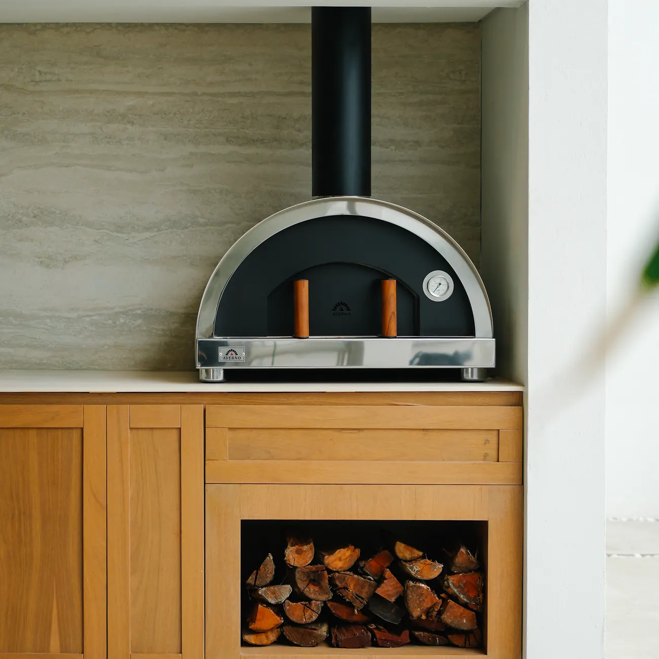 Horno Averno Firenze Standard negro con chimenea, empotrado en un nicho con leña guardada debajo