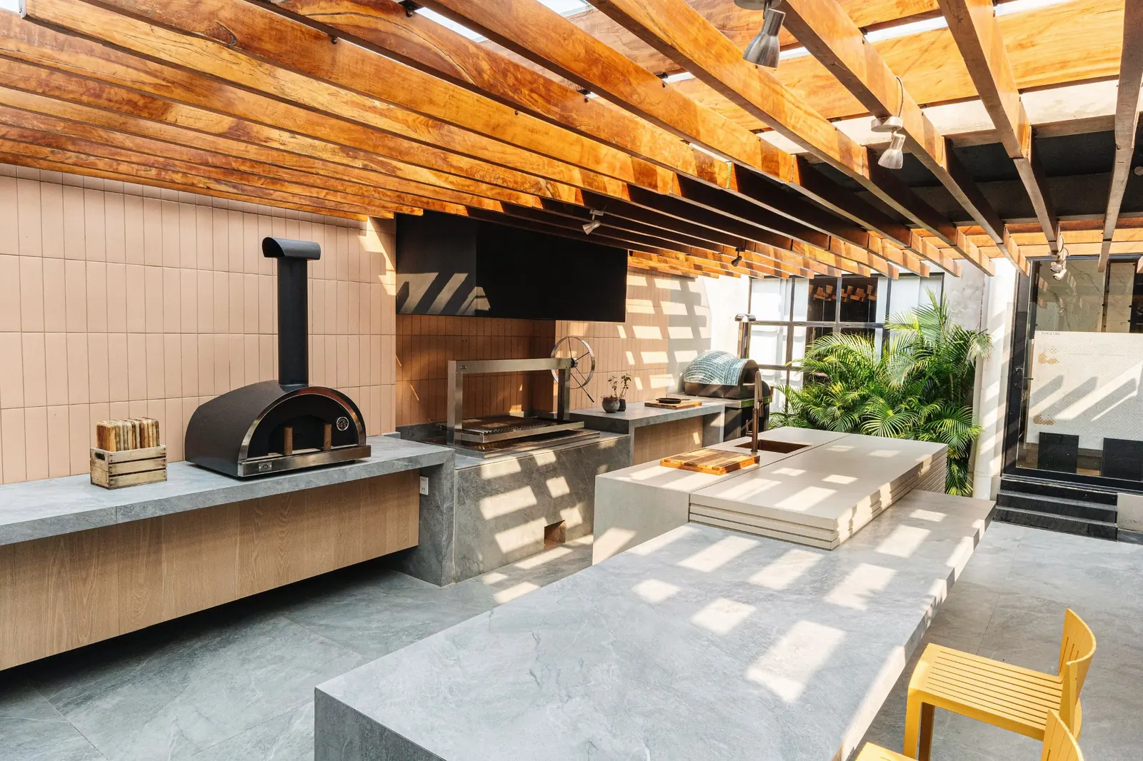 Showroom Tumpar con pérgola de vigas de madera, horno a leña, churrasquera Averno e isla de piedra sobre revestimiento rosado