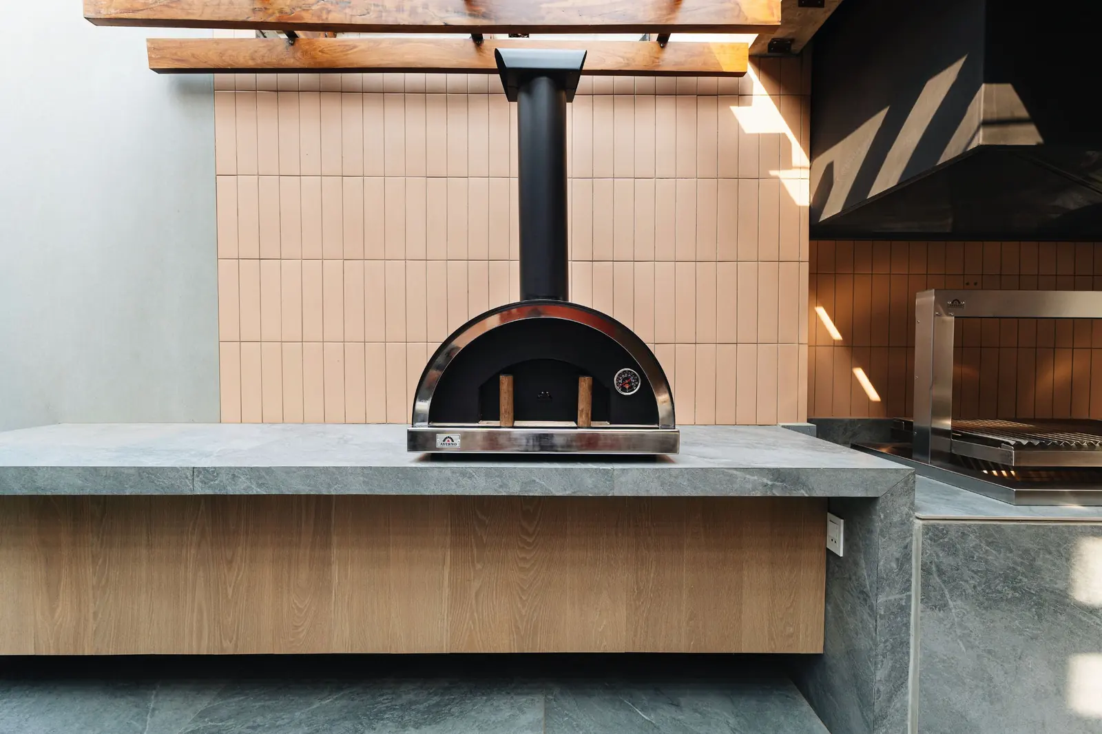 Horno Averno negro con chimenea sobre una mesada de piedra, junto a la churrasquera, en el Showroom Tumpar