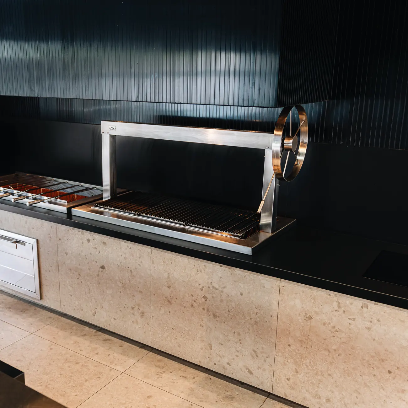 Churrasquera Averno XL junto al brochetero, sobre un mueble revestido en piedra